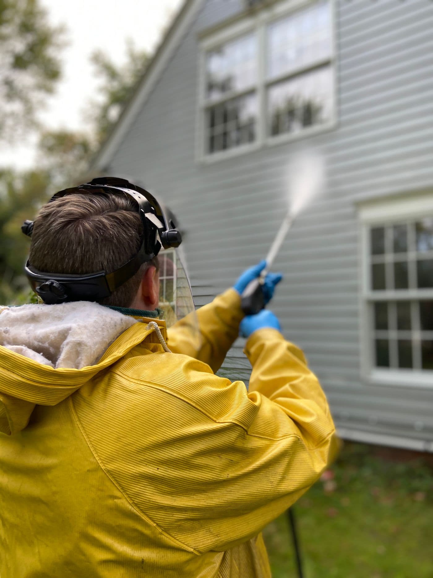 Technician in protective gear pressure washing the siding of a house