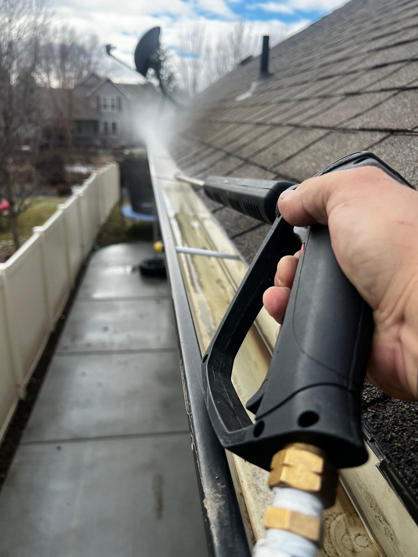 Gutter being cleaned with a pressure washer on a residential roof