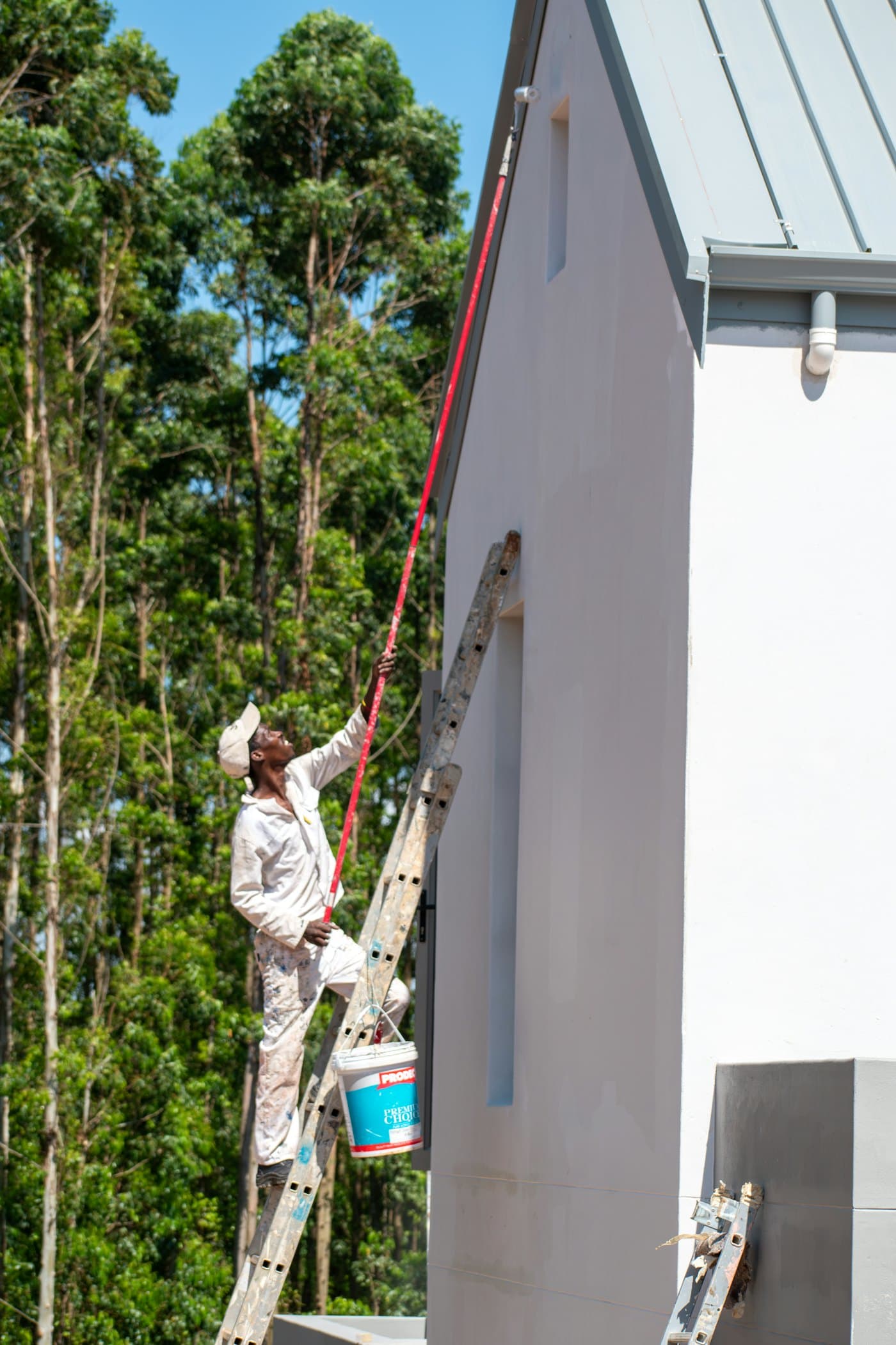 Painter on a ladder coating the exterior wall of a house